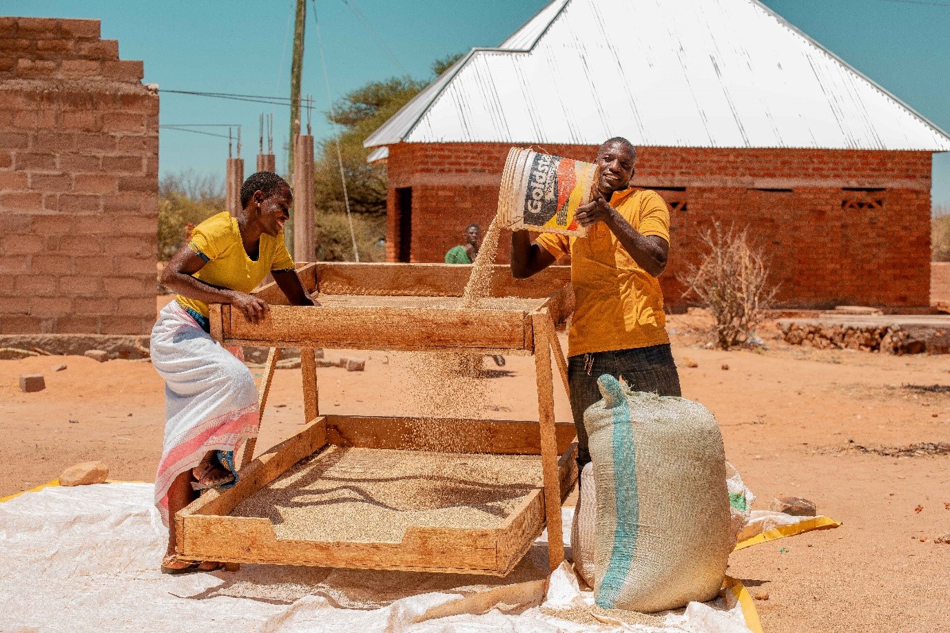 A man and woman in Tanzania milling grain using a wooden machine.